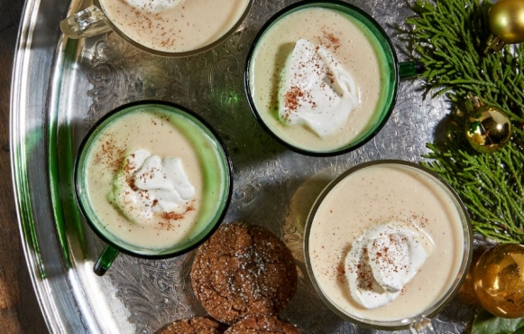 several glasses of seasonal eggnog with ornaments and cookies
